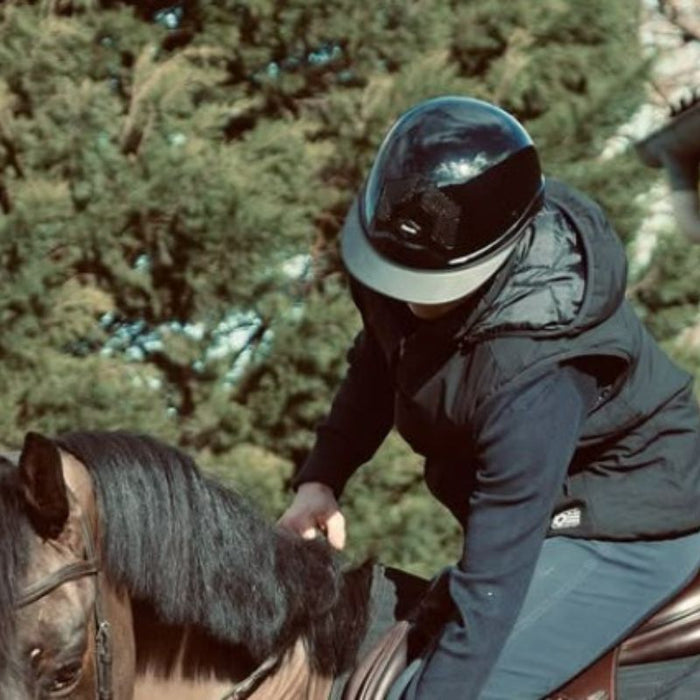 Casque d'équitation armet Flex on pour cavalier. Visière mixte. model noir mat, jugulaire marron. Vendu par fouilhoux fontainebleau. porté par une femme. 